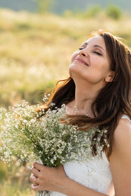 Vista laterale della donna che posa in natura con i fiori