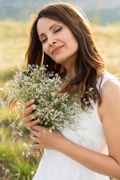 Vista laterale della donna che posa in natura con il mazzo dei fiori