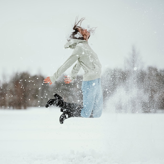Vista laterale della donna che salta all'aperto nella neve invernale