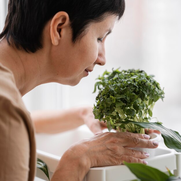 Vista laterale della donna che sente l'odore della pianta d'appartamento