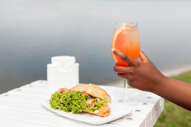 Vista laterale della donna che tiene cocktail all'aperto con panino