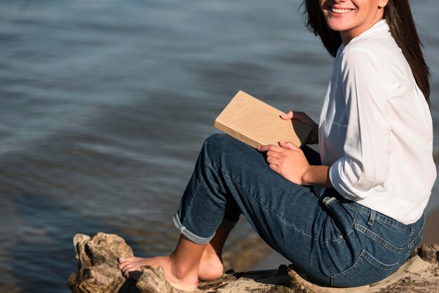 Vista laterale della donna che tiene il libro in spiaggia