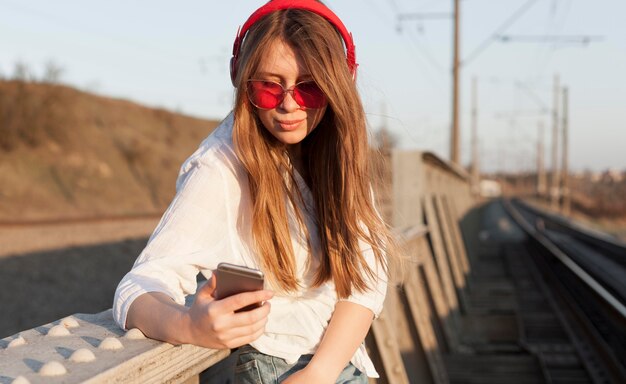 Vista laterale della donna con gli occhiali da sole e le cuffie che tengono smartphone