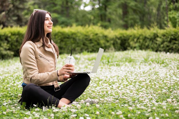 Vista laterale della donna con il computer portatile all'aperto in natura