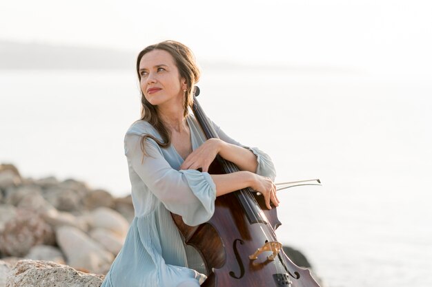 Vista laterale della donna con il violoncello sulle rocce all'aperto