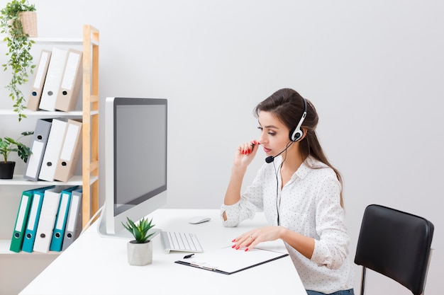 Vista laterale della donna con la cuffia avricolare che lavora allo scrittorio