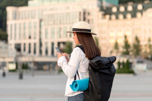 Vista laterale della donna con lo smartphone che viaggia con lo zaino