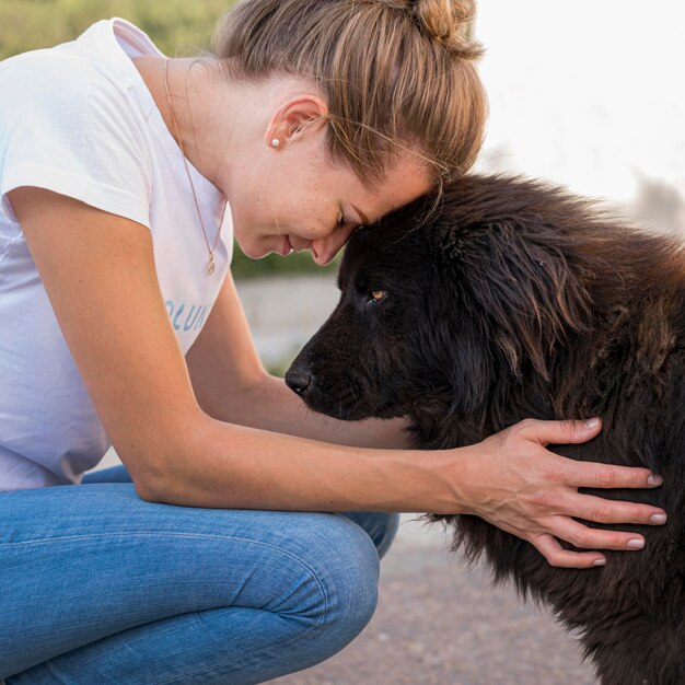 Vista laterale della donna con soffice cane nero all'aperto