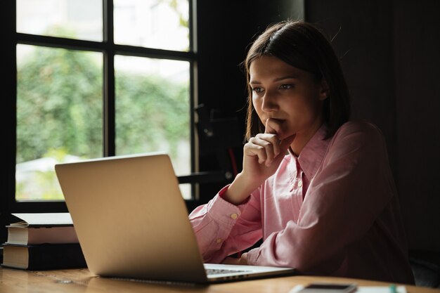 Vista laterale della donna concentrata che si siede dalla tabella in caffè