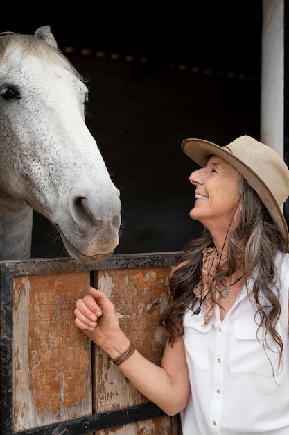 Vista laterale della donna contadina con il suo cavallo al ranch