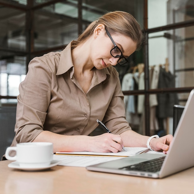 Vista laterale della donna di affari che lavora allo scrittorio con il computer portatile