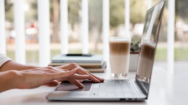 Vista laterale della donna di affari che lavora con il computer portatile e che mangia caffè