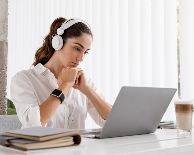 Vista laterale della donna di affari che lavora con il computer portatile e le cuffie