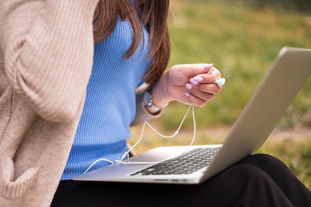 Vista laterale della donna fuori con il computer portatile e le cuffie