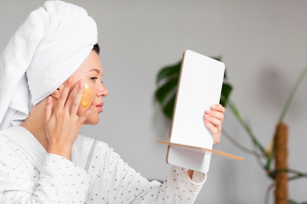 Vista laterale della donna in accappatoio che applica la cura della pelle con un asciugamano sulla testa