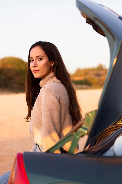 Vista laterale della donna in posa all'aperto nel bagagliaio della sua auto