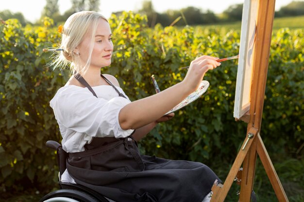 Vista laterale della donna in sedia a rotelle con tela e tavolozza