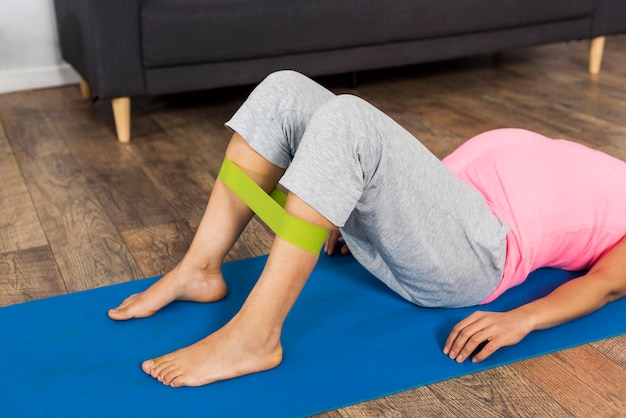 Vista laterale della donna incinta a casa che si esercita con la fascia elastica sulla stuoia