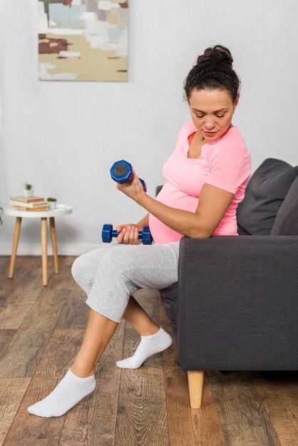 Vista laterale della donna incinta a casa con i pesi