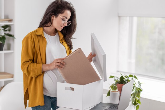 Vista laterale della donna incinta che organizza la scatola a casa