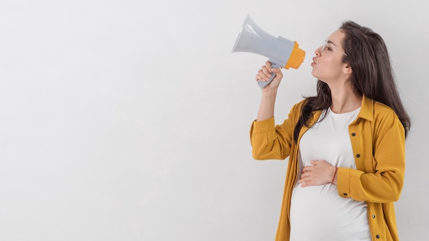 Vista laterale della donna incinta che parla tramite il megafono