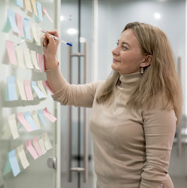 Vista laterale della donna nella scrittura dell'ufficio sulle note appiccicose