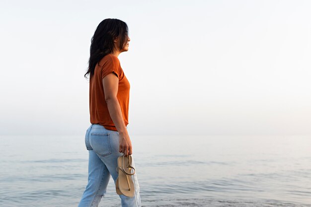 Vista laterale della donna pensierosa che fa una passeggiata sulla spiaggia