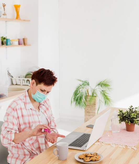 Vista laterale della donna più anziana che disinfetta le sue mani prima del lavoro a casa