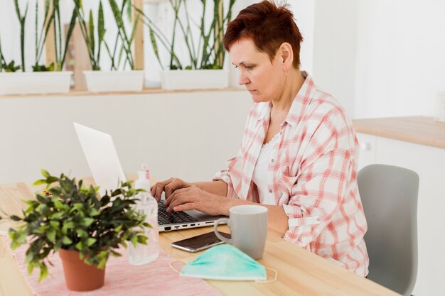 Vista laterale della donna più anziana che lavora al computer portatile dalla casa