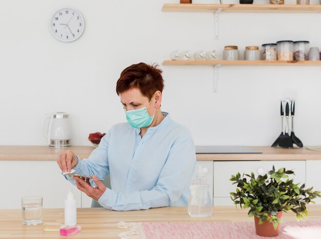 Vista laterale della donna più anziana con la mascherina medica che disinfetta il suo smartphone