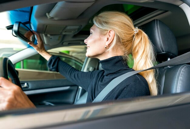 Vista laterale della donna più anziana di affari che registra il suo specchio di automobile