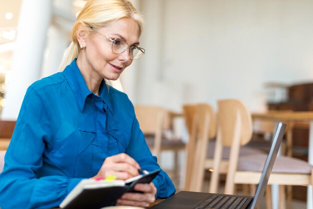 Vista laterale della donna più anziana di affari con gli occhiali che lavorano al computer portatile