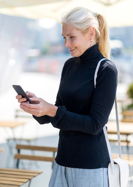 Vista laterale della donna più anziana di affari su smartphone all'aperto