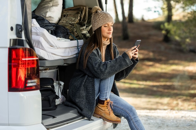 Vista laterale della donna seduta nel bagagliaio dell'auto durante un viaggio su strada e utilizza lo smartphone