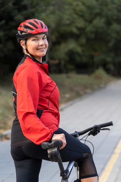 Vista laterale della donna senior di smiley all'aperto equitazione bicicletta
