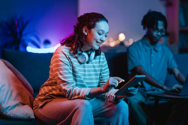 Vista laterale della donna sorridente a casa utilizzando cuffie e tablet