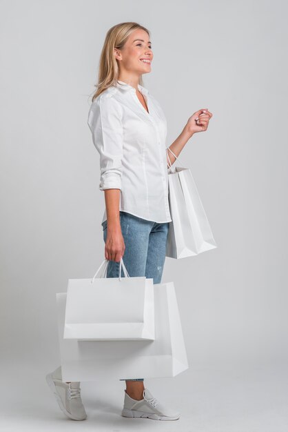 Vista laterale della donna sorridente che tiene un sacco di borse della spesa