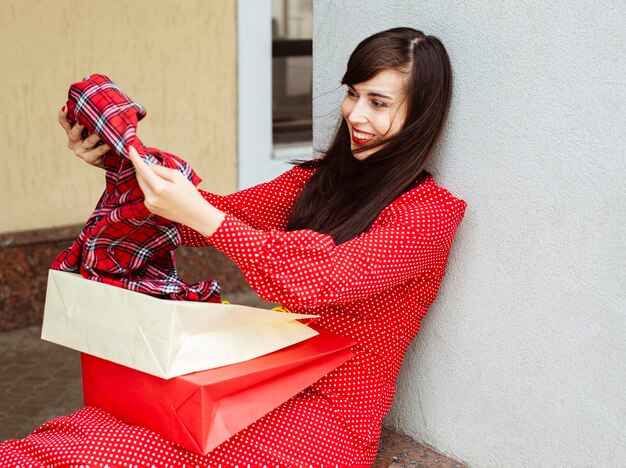 Vista laterale della donna sorridente con borse della spesa e abbigliamento in vendita