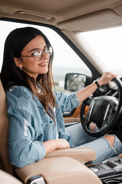 Vista laterale della donna sorridente con gli occhiali che viaggiano da soli in auto