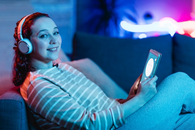 Vista laterale della donna sorridente utilizzando tablet e cuffie a casa