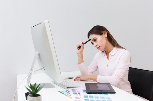 Vista laterale della donna sul lavoro che pensa e che esamina computer