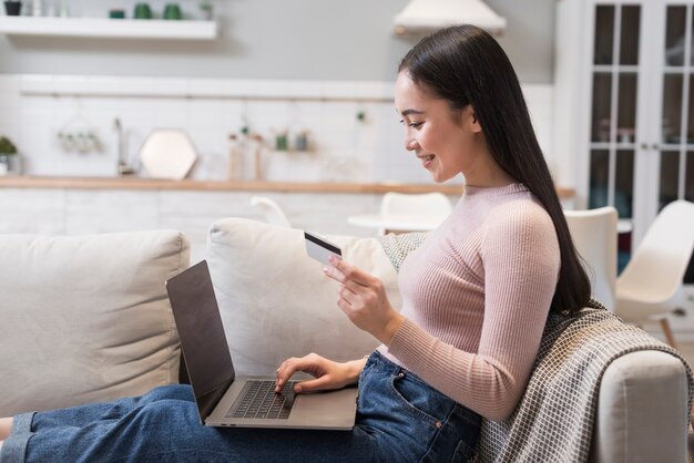 Vista laterale della donna sul sofà che compera online