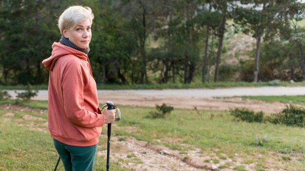 Vista laterale della donna turistica anziano con bastoncini da trekking