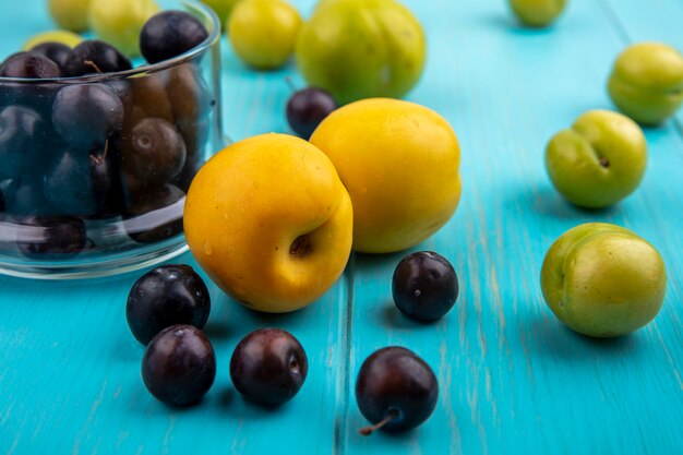 Vista laterale della frutta come bacche di uva prugne e nectacots con ciotola di acini d'uva su sfondo blu