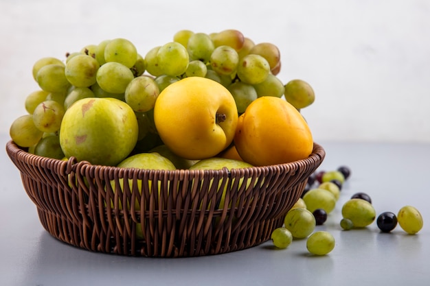 Vista laterale della frutta come nectacots verde pluots uva nel carrello con acini d'uva su superficie grigia e sfondo bianco