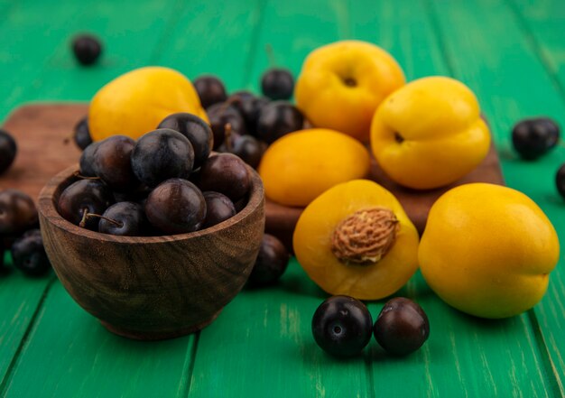 Vista laterale della frutta come prugnole e albicocche nella ciotola e sul tagliere su sfondo verde