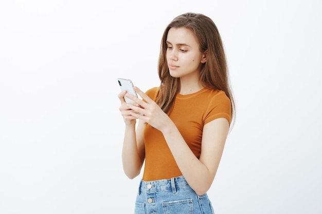 Vista laterale della giovane donna attraente messaggistica, guardando lo smartphone mentre si modifica la foto con l'app mobile