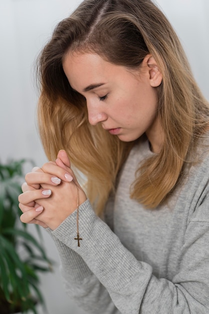 Vista laterale della giovane donna che prega con collana croce