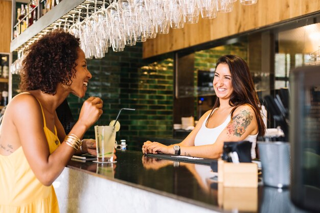 Vista laterale della giovane donna che sorride con il barista femminile al contatore della barra