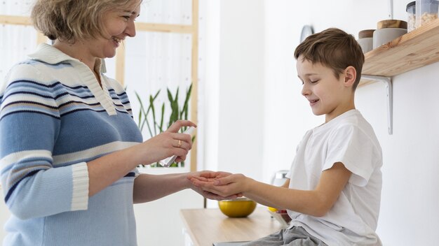 Vista laterale della madre che dà a figlio disinfettante per mani